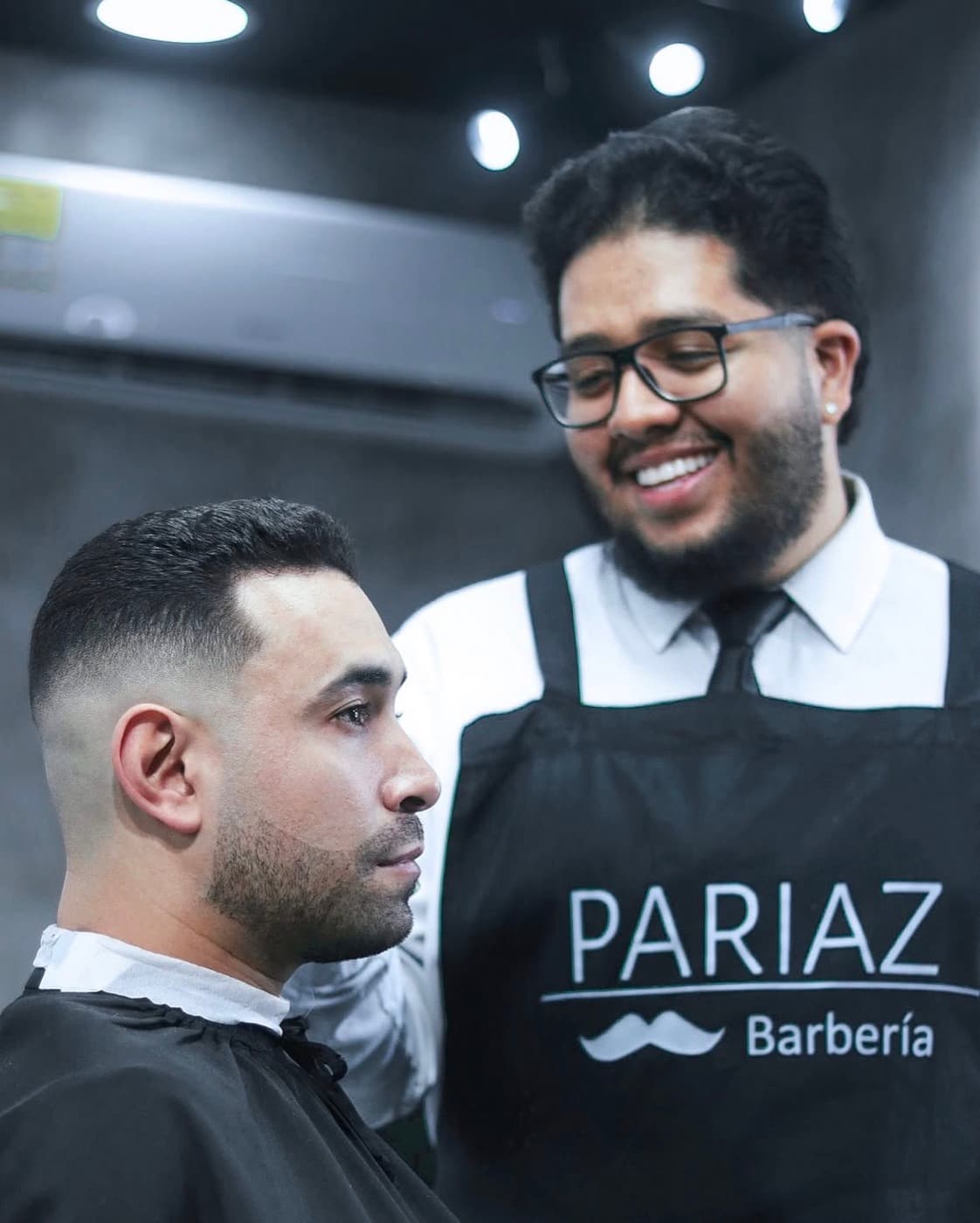 Barbero de Pariaz sonriendo junto a un cliente